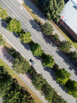 Aerial view of a road with a single car driving past lush green trees and a modern building in Oulu, North Ostrobothnia, Finland.