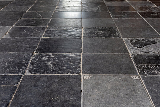 Close-up view of an old stone floor inside a historic church, with dark floor tiles, worn textures and engraved grave slabs. Interior image showing aged stonework, heritage detail and quiet architectu
