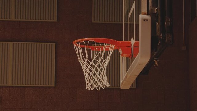 Static view of a basketball hoop and net inside a dim gymnasium.