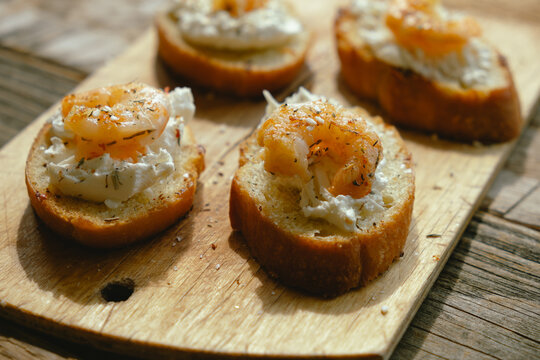 Bruschetta or crostini with cream cheese and shrimp on wooden board. Tasty snacks.