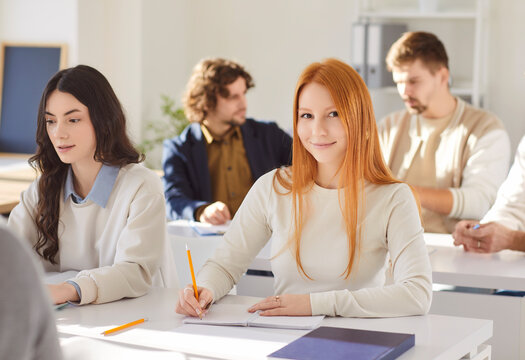 Portrait of happy redhead woman student during lesson in high school, writing in notebook for learning and education in a supportive classroom setting with focus and dedication daily.