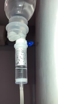 Close-up of an IV drip bag and saline fluid dripping into the chamber in a hospital or medical setting.