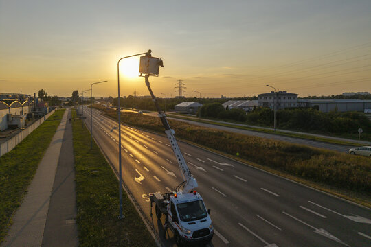 Aerial view of a worker in a bucket truck servicing a street lamp during golden hour along a road in Krakow, Lesser Poland Voivode, Poland.