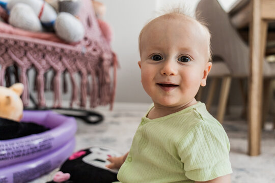 Smiling baby in a green shirt sits on the floor