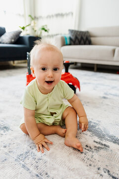Smiling baby sit on rug in bright living room