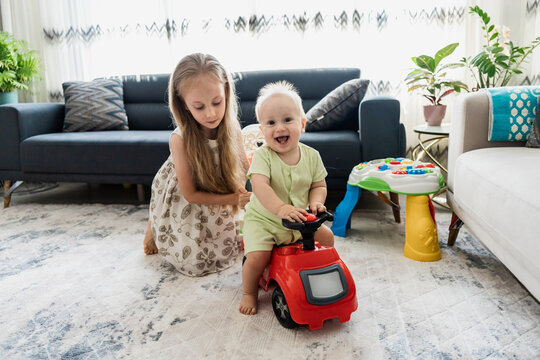 Siblings play with ride-on toy car at home