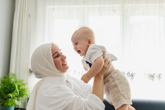 Muslim mother lift happy baby at home by window