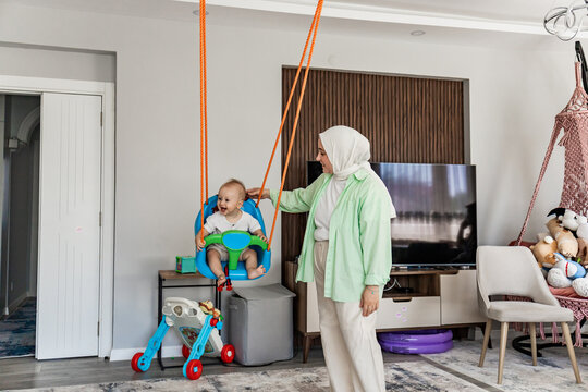 Mother pushes toddler on indoor swing at home