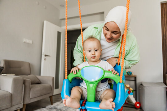 Mother helps toddler on indoor swing at home