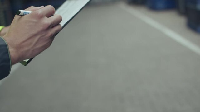 Worker writing notes on clipboard in storage warehouse