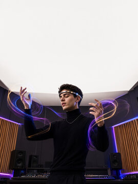A composer wearing a neural interface meditates in a professional studio, materializing sound frequencies as glowing spirals around his hands