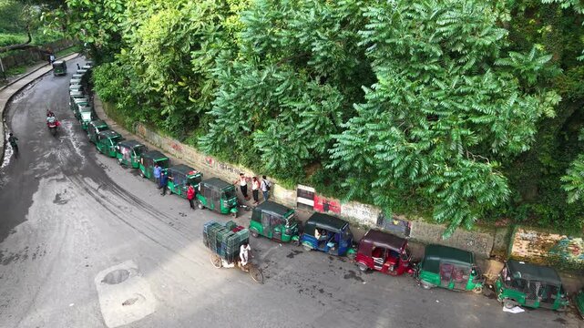 Chittagong, Bangladesh - 03 August 2026: Aerial view of a line of green auto-rickshaws parked along a road near the lush trees of CRB Chittagong.
