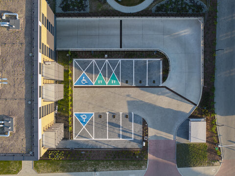 Aerial view of a modern parking lot with designated electric vehicle charging stations and accessible parking spaces located next to an office building in Krakow, Lesser Poland Voivode, Poland.