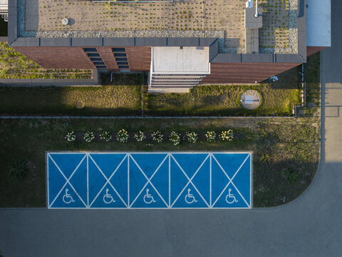 Aerial view of blue-painted accessible parking spaces next to a modern brick office building with a green roof in Krakow, Lesser Poland Voivode, Poland.