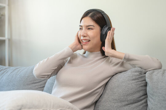 Relaxed female sitting on the sofa in the living room listen to music via headphone.