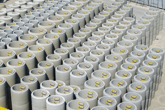 Aerial view of rows of stacked concrete manhole rings with yellow metal steps arranged in a storage yard in Poland.