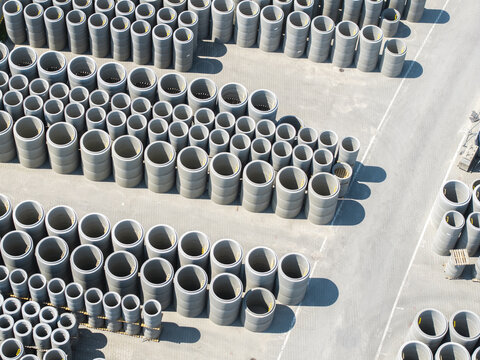 Aerial view of rows of concrete pipes and cylindrical precast elements stored in an industrial yard in Poland.