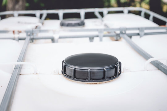 Close-up of plastic IBC tote tank lids and metal cage frame outdoors, used for bulk liquid storage and water collection. Agriculture concept.