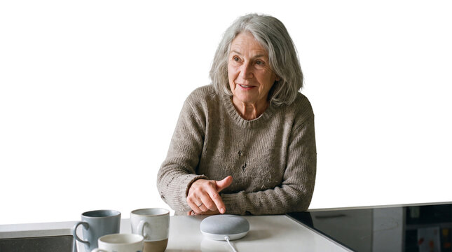 Senior woman at home using smart speaker with mugs. Senior person talking to voice assistant. Happy elderly lady listening to Internet of Things. Communication device.