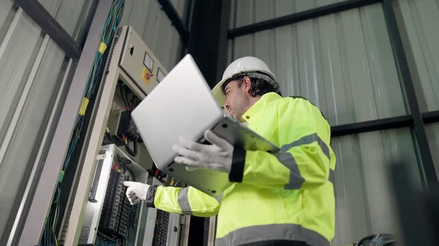 Preventive maintenance Electrical technician using laptop working electrical system inspection beside control panel in factory. diagnostics, troubleshooting, safety, preventive service.