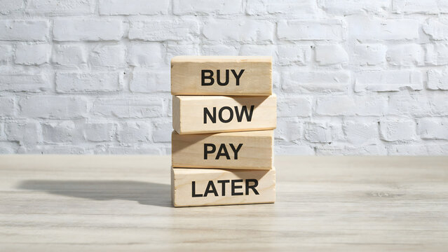 A stack of wooden blocks with the words buy now pay later on a table