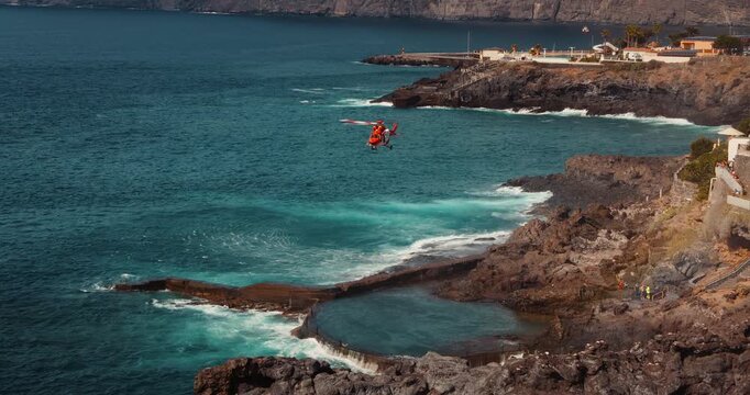 TENERIFE, CANARY ISLANDS, SPAIN, 2023 April: Medical rescue helicopter hovers above stromy sea near cliff edge.
