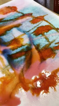 Woman using a dropper to apply red watercolor ink onto wet paper surface. Abstract painting process with vibrant color blending and fluid artistic ink technique.