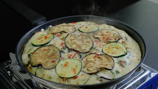 Cooking vegetables like zucchini and eggplant in a creamy sauce inside a large skillet on an electric hot plate in a kitchen, Cooking location, daytime.