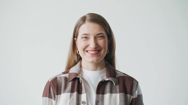 Smiling young Caucasian woman looking at camera against clean bright background. Female wearing casual plaid shirt and expressing genuine happiness with natural confident portrait pose.
