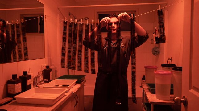 Person hanging wet medium format film negatives to dry in a darkroom under red safelight