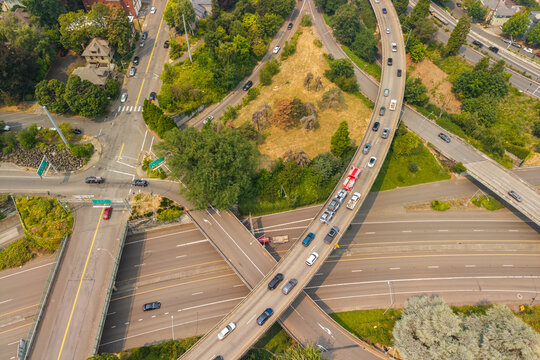 Aerial view of a highway interchange with cars driving on elevated roads surrounded by green trees and urban infrastructure in Portland, Oregon, United States.