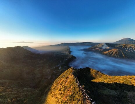Aerial view of Mount Bromo with volcanic craters rising above a sea of clouds under golden morning light in Tosari, East Java, Indonesia.