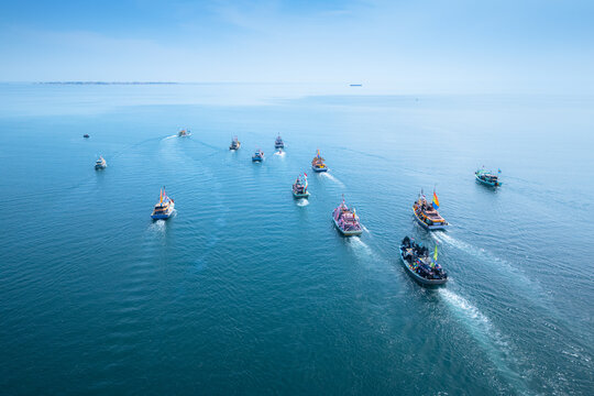 Aerial view of a fleet of colorful traditional fishing boats sailing across the calm blue waters of the Mayangan port area in Probolinggo, East Java, Indonesia.