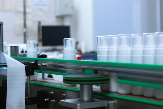 Factory conveyor line: row of white plastic dispenser bottles moves along green production line