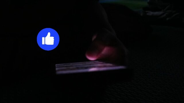 Person using a smartphone in the dark with a blue thumbs up icon overlay.