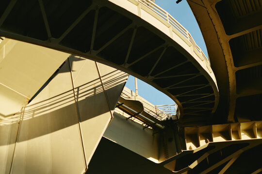 Low angle view of modern concrete bridge structure with curved overpass under blue sky. Image represents urban infrastructure development and civil engineering projects, low angle view