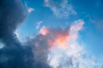 Fototapeta premium Pink and grey clouds float in a bright blue sky during sunset. Evening light, natural background, peaceful atmosphere. High quality photo
