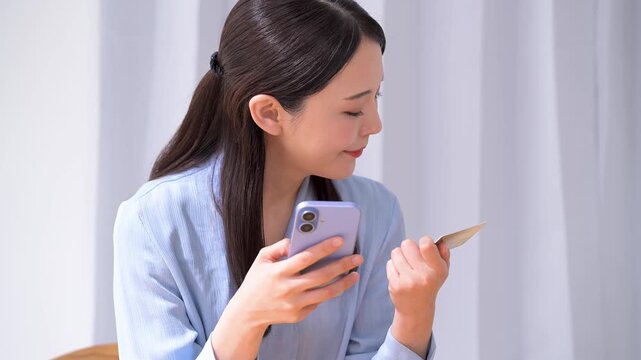クレジットカードを見ながらスマホを操作する女性