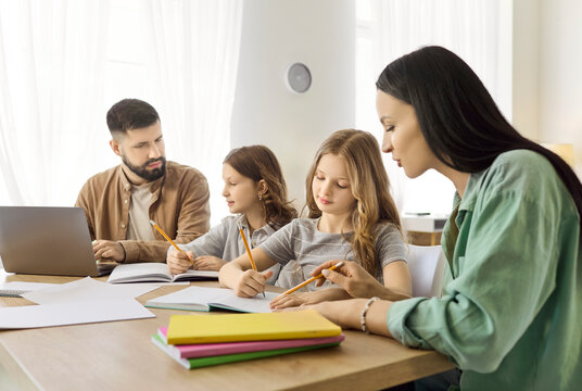 Family parents assist children and daughters with homework. At home father uses a laptop while mother guides studying at the table, encouraging focus. Concept shows supportive family learning