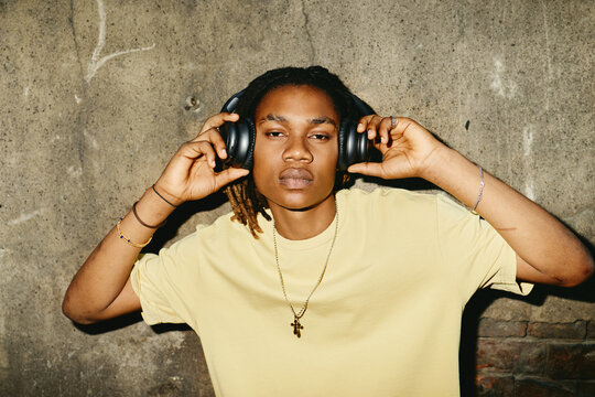 Portrait of young Black man wearing headphones outdoors, listening to music. Image represents youth culture and is ideal for audio equipment marketing campaigns, medium shot