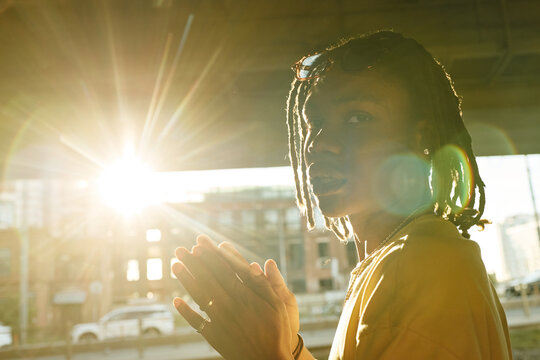 Portrait of young Black man standing outdoors with hands together during sunset, representing youth culture and mindfulness. Image suitable for Gen Z lifestyle marketing campaigns