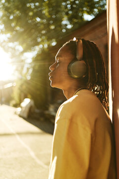 Young African American man listening to music in headphones outdoors with closed eyes, representing mental wellbeing and youth lifestyle, vertical