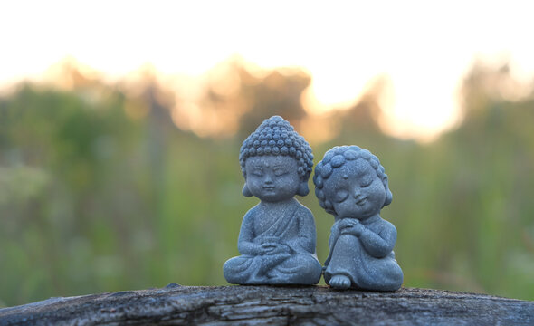 beautiful miniature asian style girl and boy figurines and flowers close up outdoor, abstract natural background. cute little Buddhist monk figurines in garden. meditation, yoga concept. soft focus