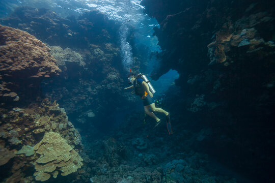 Scuba diver swimming inside a dramatic coral reef cave canyon underwater