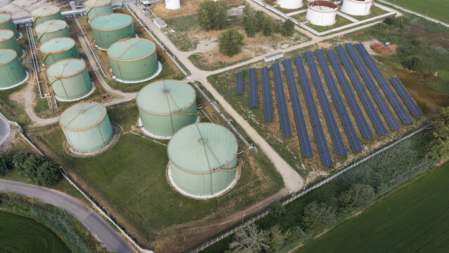 Aerial view of a petroleum storage facility with large green cylindrical tanks and a solar panel array in Lacchiarella, Lombardy, Italy.