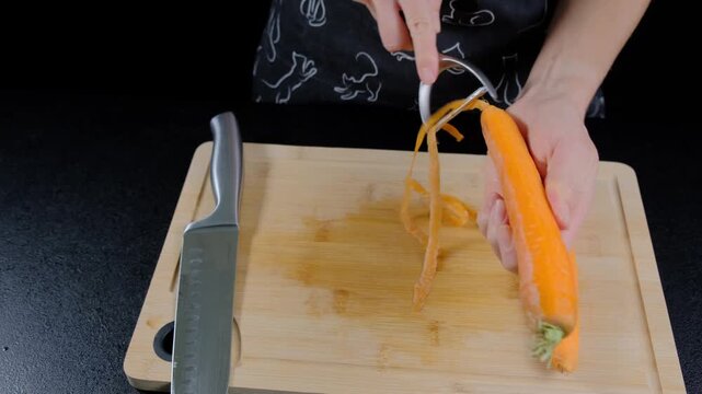 A person in an apron uses a mandoline slicer to cut carrots into thin strips on a wooden cutting board in a Cooking kitchen during daytime.