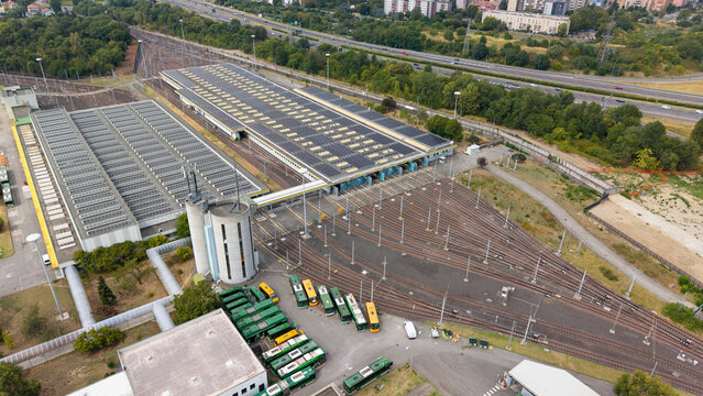 Aerial view of the ATM Campus bus depot featuring large maintenance buildings with solar panels, multiple bus parking bays, and railway tracks in Milano, Lombardia, Italy.