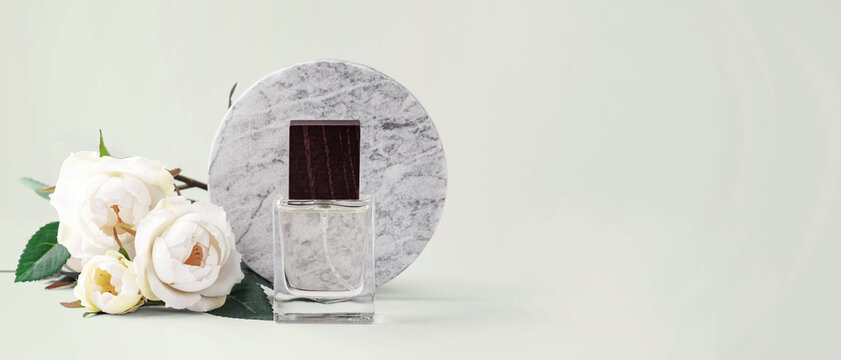 Glass perfume or cosmetic spray bottle with wooden cap and white roses decoration with a round marble background on light green background
