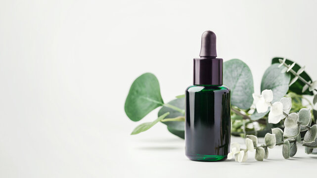 Green essential oil dropper bottle with eucalyptus leaves on light green background