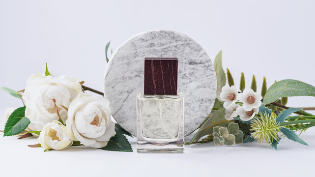 Perfume bottle with wooden cap, white roses and green leaves decoration with a round marble podium on white background